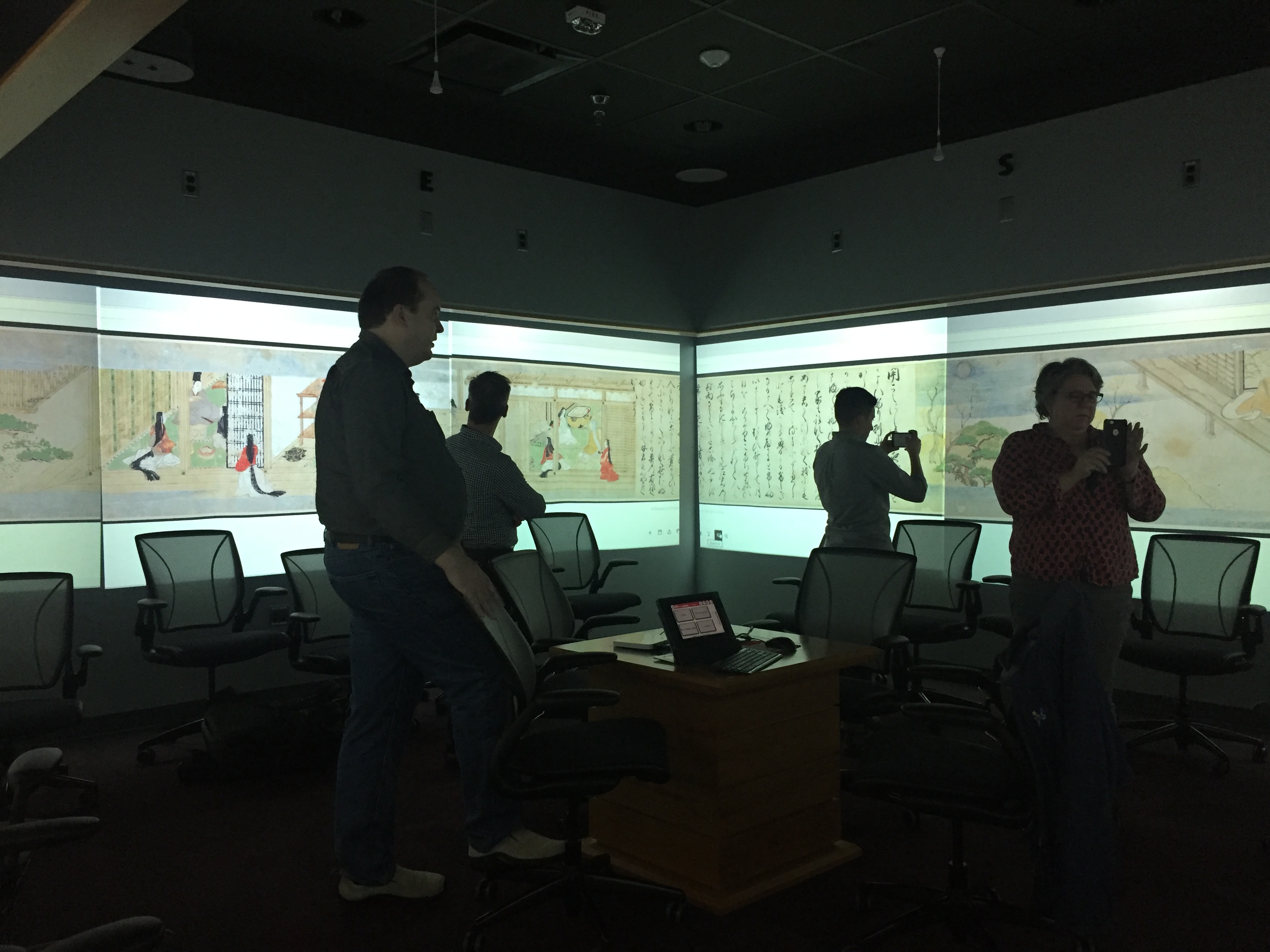 Harvard staff explore an interactive classroom with projectors displaying IIIF assets on all walls